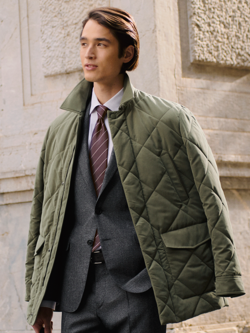 Canali sage green quilted jacket layered over a grey tailored suit, striped shirt and tie, showcasing refined outerwear and craftsmanship.
